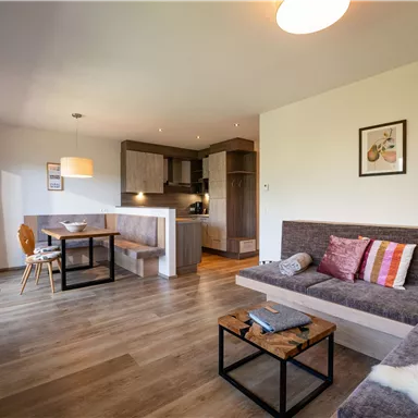 A modern living room with a cozy couch and dining table. The kitchen is open and well-equipped, with warm lighting and appealing decoration.