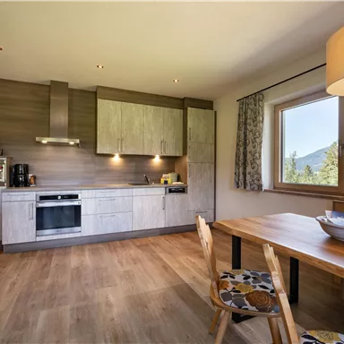 Modern kitchen with wooden surfaces and a large window front. A wooden dining table complements the space and provides a cozy atmosphere.