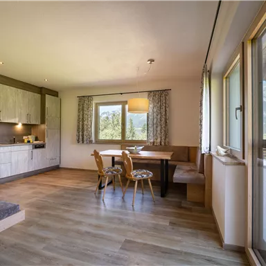 A modern kitchen with wooden surfaces and a cozy dining area. Large windows offer a view of the mountains.