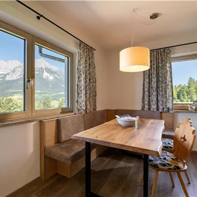 A bright dining area with a wooden chair and a large table. Through the windows, there is a beautiful view of the mountains and nature.
