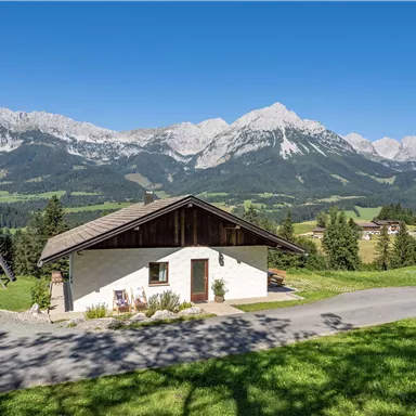 A cozy house in a picturesque mountain landscape. Majestic mountains rise in the background under a blue sky.