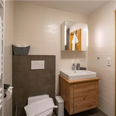 A modern bathroom with a bright tile design and a wooden wash basin. Towels and care products are visible.