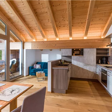 A modern, bright apartment with a wooden ceiling and open space. The kitchen is well-equipped, and there is a cozy living area.