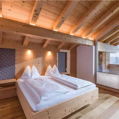 A cozy bedroom with wooden walls and a large window. There are two beds with white duvet covers and an inviting atmosphere.