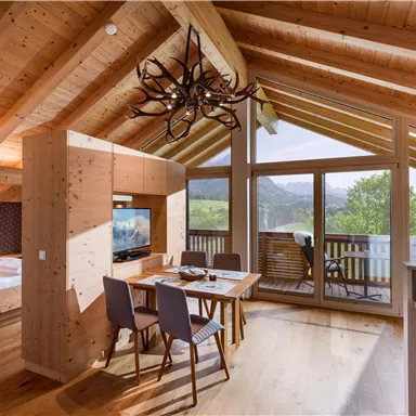 A cozy room with a wooden ceiling and large windows. The dining area is modernly furnished and offers a view of the landscape.
