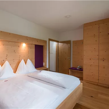 A modern bedroom with wooden paneling and a double bed. The walls are light and the room feels cozy and inviting.