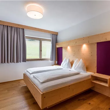 A cozy bedroom with a large bed and wooden decor. The room has a window overlooking nature and soft lighting.