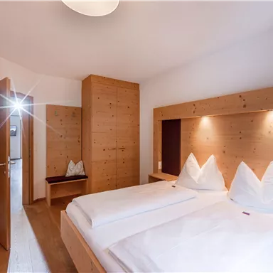 A cozy bedroom with two beds and modern wooden furniture. The room is brightly lit and has an inviting atmosphere.