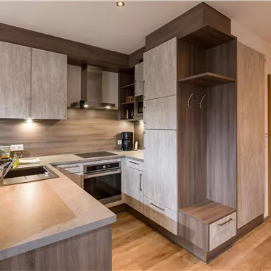 A modern kitchen with wood fronts and elegant surfaces. It is well equipped with a stove, an oven, and a space for storage.