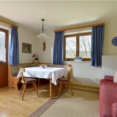Ein gemütlicher Essbereich mit einem runden Tisch und Holzmöbeln. Große Fenster lassen viel Licht herein und bieten einen Blick ins Freie.