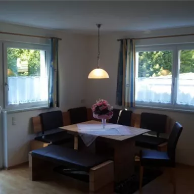 A cozy dining area with a round table and a bench. Large windows let in plenty of light and offer a view of the garden.