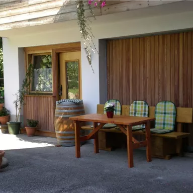 A cozy entrance area with a wooden table and chairs. Various plants in pots and a large barrel create an inviting atmosphere.