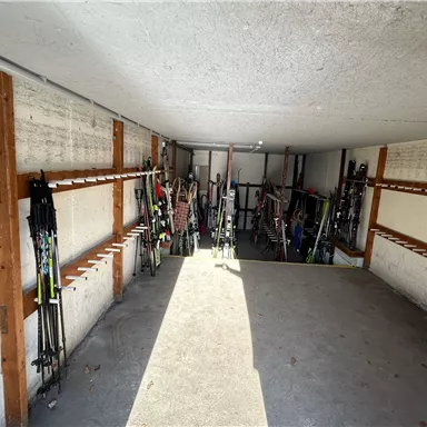 A room with several ski poles, neatly lined up against the walls. The floor is gray and the room is well lit.