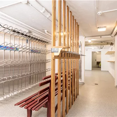 A modern hallway with bicycle racks and wooden shelves. The walls are painted light, and the floor is made of gray material.