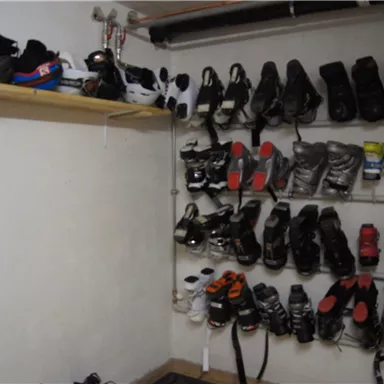 Ein Raum mit verschiedenen Ski- und Snowboardschuhen, die ordentlich an einer Wand hängen. Oben ist ein Regal mit weiteren Paaren von Schuhen.