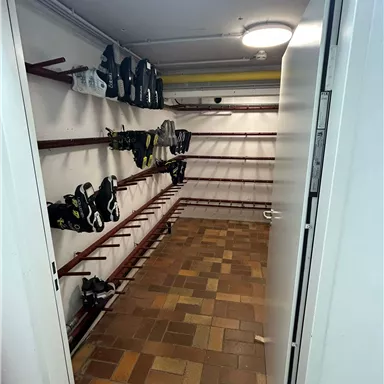 A small room with shelves on which ice skates are neatly arranged. The floor is tiled and the light is bright.