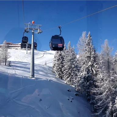 A ski lift gondola is traveling over a snow-covered landscape. The trees are covered with snow and the sky is blue.