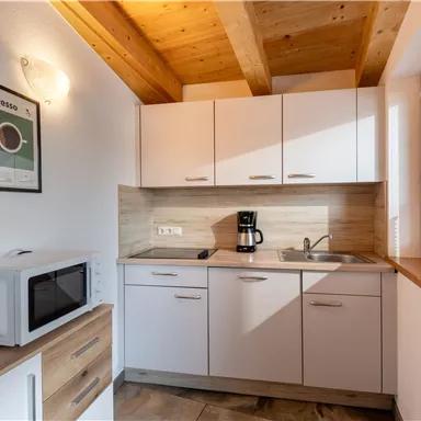 A modern kitchen with wooden details and bright cabinets. On the countertop, there is a coffee machine and a microwave.