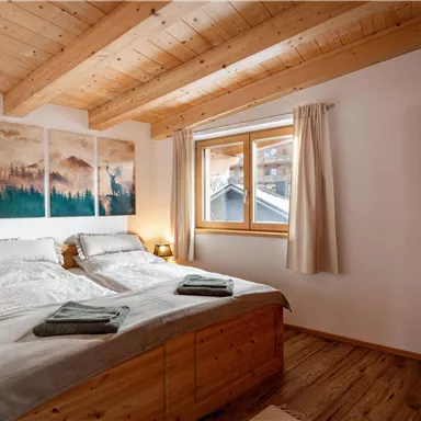 A cozy bedroom with two wooden beds and natural accents. Large windows bring plenty of light into the room.