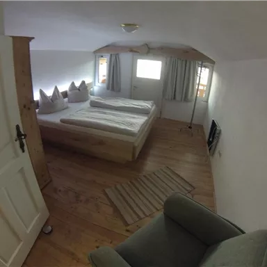 Ein gemütliches Schlafzimmer mit zwei Einzelbetten und Holzfußboden. Die Fenster lassen viel Tageslicht herein, und es gibt einen kleinen Sitzbereich.