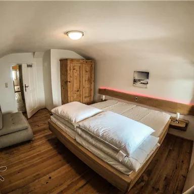 Ein gemütliches Schlafzimmer mit einem großen Bett und Holzfußboden. Es gibt einen Kleiderschrank und eine kleine Sitzecke.