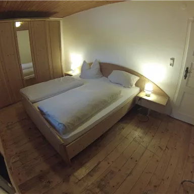 Ein gemütliches Schlafzimmer mit zwei Betten und Holzboden. Es gibt einen Kleiderschrank und eine gemütliche Nachttischlampe.
