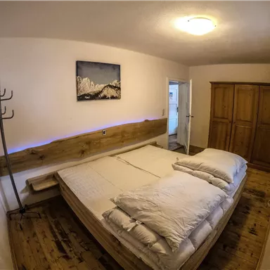 Ein gemütliches Schlafzimmer mit einem großen Bett und hellen Kissen. An der Wand hängt ein Bild von Bergen, und es gibt einen Holzschrank sowie eine Garderobe.