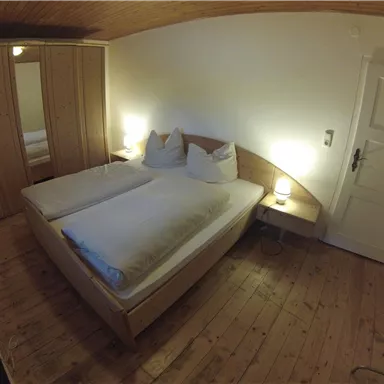 Ein gemütliches Schlafzimmer mit einem Doppelbett und Holzfußboden. Es gibt einen Kleiderschrank und sanfte Beleuchtung.