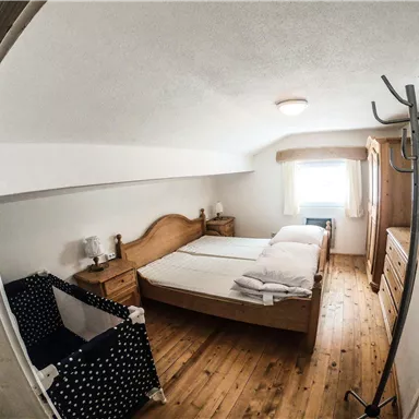 Ein helles Schlafzimmer mit zwei Betten und Holzfußboden. Es gibt einen Kleiderschrank und eine gemütliche Sitzecke.