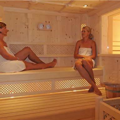 Two women are relaxing in a bright wood sauna. The atmosphere is cozy and inviting.