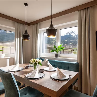 An inviting dining area with a wooden table and stylish chairs. Large windows provide a view of the green landscape and the mountains.