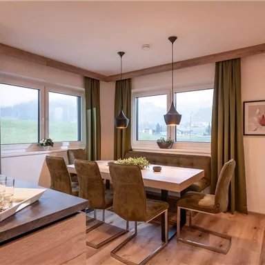 A modern dining room with a large table and comfortable chairs. Natural light streams through the windows, and the curtains are in a beautiful shade of green.