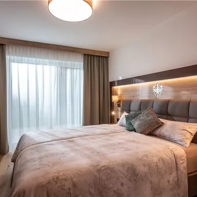 A modern bedroom with a large bed and soft colors. Large windows let in plenty of daylight.