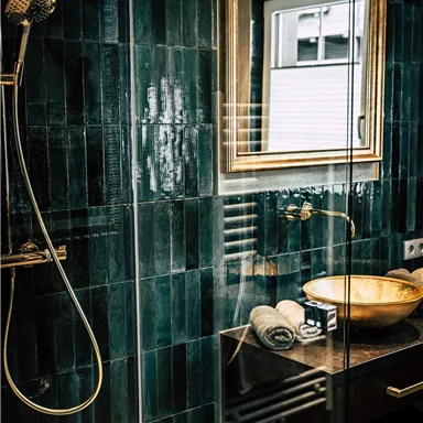 A modern bathroom with green tiles and an elegant sink. The large mirror and the shower create a stylish atmosphere.