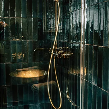 An elegant shower featuring shiny dark tiles. The shower head and fixtures are designed in a gold color.