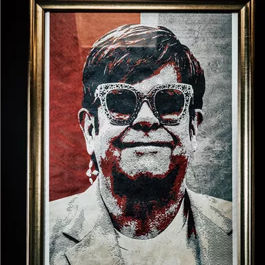 An artistic portrait of a person with wide glasses and a smile. The background is colored in red and gray.