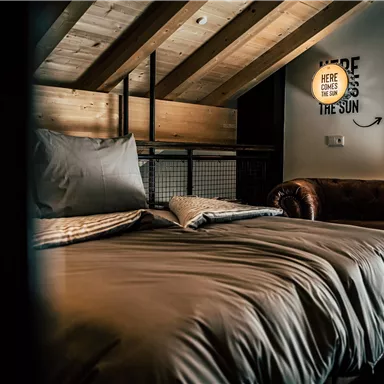 A cozy bedroom with a large bed and a leather couch. Wood paneling and soft lighting create a relaxed atmosphere.