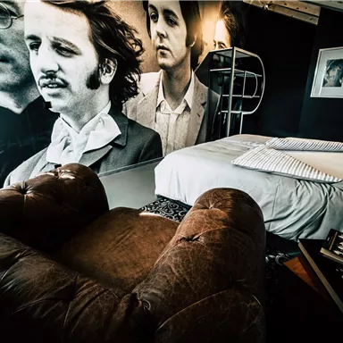 A stylish room with a cozy armchair and a double bed. Large portraits of musicians hang on the walls.