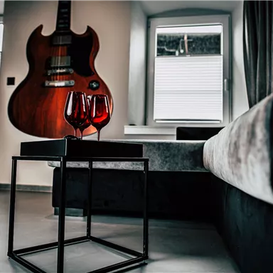 A stylish living room with a black table and two red wine glasses. In the background, an electric guitar is hanging on the wall.