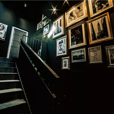 A stairwell with dark walls and a modern railing. The walls are adorned with framed pictures.