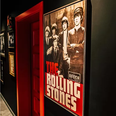 A poster of the Rolling Stones on a dark wall. The door in the background is red.