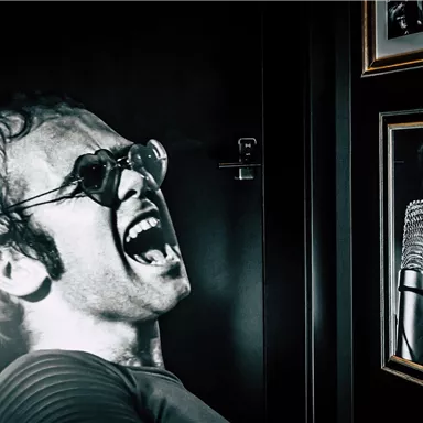 An impressive mural of a famous person wearing sunglasses, passionately singing. Next to the image are two photographs and a microphone frame.