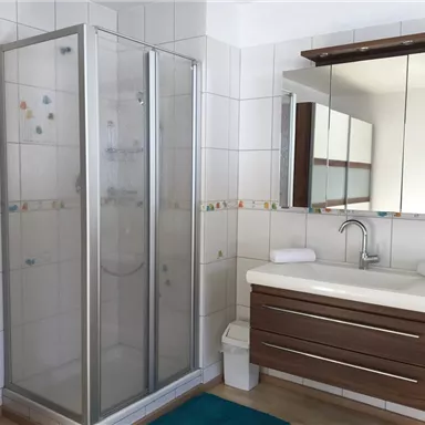 Ein modernes Badezimmer mit einer Dusche und einem eleganten Waschbecken. Die Fliesen sind hell und die Einrichtung ist schlicht und stilvoll.