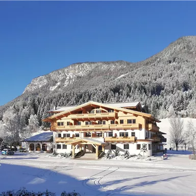 A charming hotel in winter, surrounded by snow-covered mountains and trees. The clear blue sky creates a soothing atmosphere.