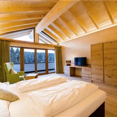 A modern bedroom with wooden ceilings and a large window. The room is brightly and cozily furnished.