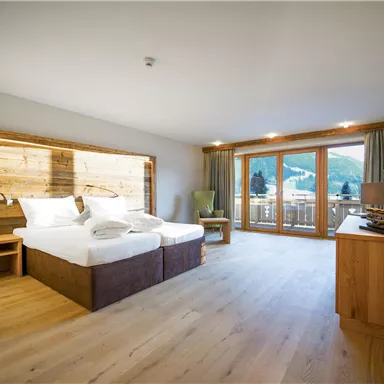 A modern hotel room with two beds and wooden accents. Large windows offer a view of the surrounding landscape.