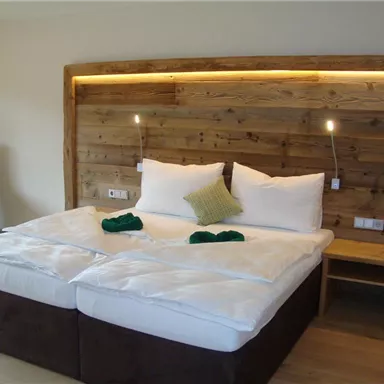 A cozy bedroom with two beds and wooden paneling on the wall. The soft lighting creates a pleasant atmosphere.