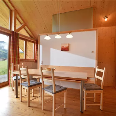 A bright, modern dining room with wooden paneling. Large windows offer a view of the surrounding landscape.