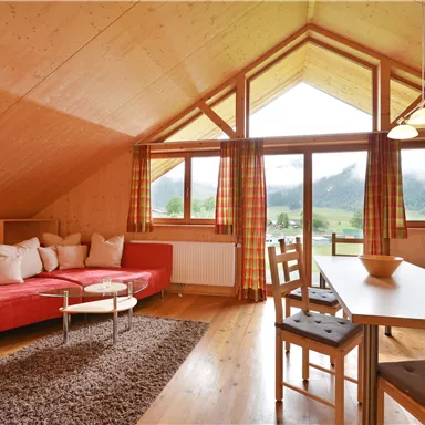 A cozy living room with a red sofa and a dining table. Large windows provide a beautiful view of the mountains and let in plenty of light.