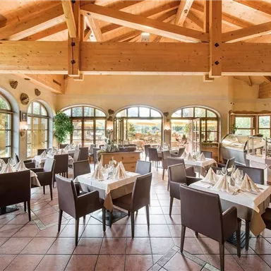 An elegant restaurant setting with wooden beams and large windows. Tables are beautifully set and invite you to dine.